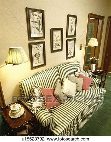 Stock Image - Group of pictures on wall above striped sofa in traditional living room. Fotosearch