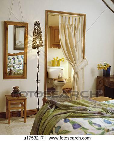 Handmade metal barbed-wire standard lamp beside mirror in bedroom with green throw on bed and cream curtain on doorway to ensuite bathroom View Large Photo Image Stock Image - Handmade metal barbed-wire standard lamp beside mirror in bedroom with green throw on bed and cream curtain on doorway to ensuite bathroom. Fotosearch
