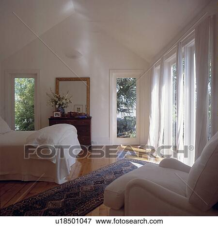 High ceilinged white bedroom with sun coming in through windows View Large Photo Image Stock Photo - High ceilinged white bedroom with sun coming in through windows. Fotosearch