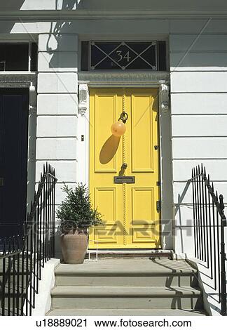 Stock Image - Iron railings on either side of steps up to yellow traditional front door. Fotosearch
