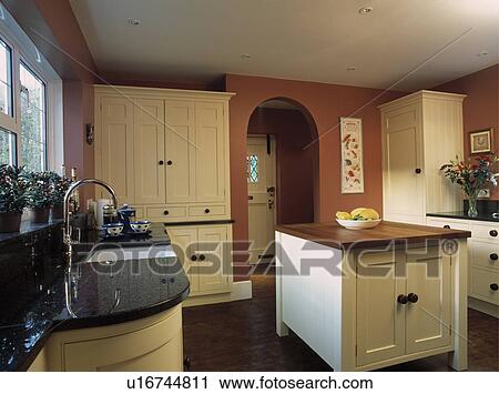 Stock Image - Island unit in terracotta kitchen with cream fitted cupboards . Fotosearch