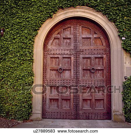 Stock Image - Ivy growing on wall above studded carved wood double doors. Fotosearch