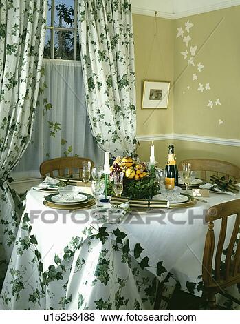 Stock Photo - Ivy patterned curtains and matching cloths on circular table set for dinner. Fotosearch