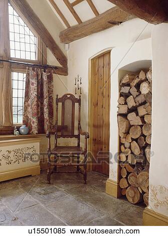 Stock Photography - Jacobean chair in corner of country hall with stone floor and logs stored in tall alcove. Fotosearch