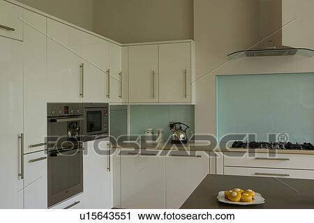 Stock Image - Kettle on worktop in modern white kitchen with turquoise wall above built-in hob. Fotosearch