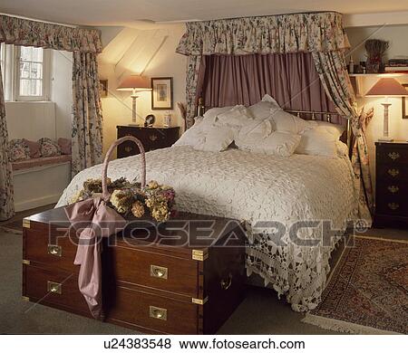 Stock Photo - Lace bedspread on bed with curtains in attic bedroom with brassbound chest at the foot of the bed. Fotosearch