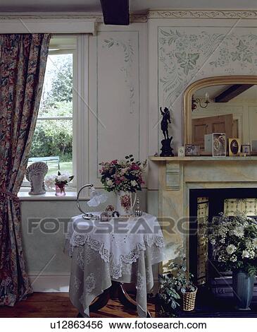 Stock Photograph - Lace cloth on circular table in cottage living room with stencilled walls. Fotosearch