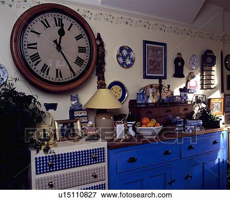 Large antique circular clock on wall above chest with checked fabric covered drawers beside old blue cupboard View Large Photo Image Stock Photo - Large antique circular clock on wall above chest with checked fabric covered drawers beside old blue cupboard. Fotosearch