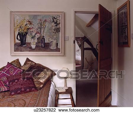 Stock Image - Large floral painting above bed with Indian silk cushions in cottage bedroom. Fotosearch