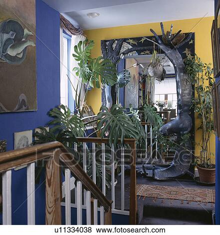 Large houseplants and modern sculpture in front of large mirror on blue and yellow landing View Large Photo Image Stock Photo - Large houseplants and modern sculpture in front of large mirror on blue and yellow landing. Fotosearch