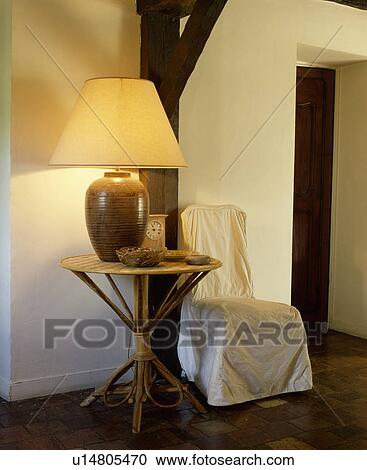 Large lighted lamp on bamboo table beside chair with white loosecover in country hall View Large Photo Image Stock Image - Large lighted lamp on bamboo table beside chair with white loosecover in country hall. Fotosearch