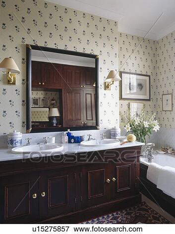 Large mirror above double white basins in mahogany vanity unit in traditional bathroom with flower patterned wallpaper View Large Photo Image Stock Photo - Large mirror above double white basins in mahogany vanity unit in traditional bathroom with flower patterned wallpaper. Fotosearch