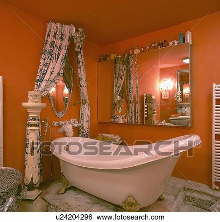 Large mirror above white rolltop slipper bath in orange bathroom with coronet curtains and ornate pedestal View Large Photo Image Stock Photograph - Large mirror above white rolltop slipper bath in orange bathroom with coronet curtains and ornate pedestal. Fotosearch