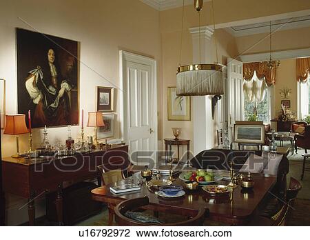 Stock Image - Large oil painting above sideboard in traditional townhouse dining room with antique table and double doors to living room. Fotosearch
