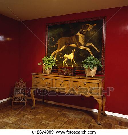 Stock Photo - Large oil painting of dogs above antique sideboard in red hall with lacquered walls. Fotosearch