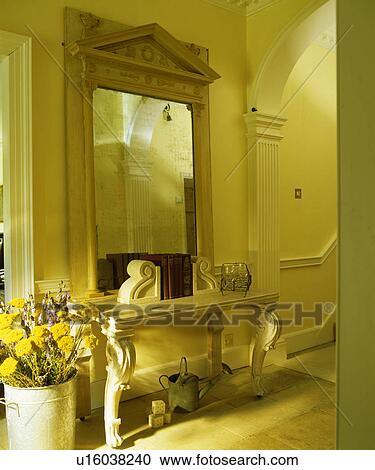 Stock Image - Large pedimented antique mirror above marble console table in cream hall. Fotosearch
