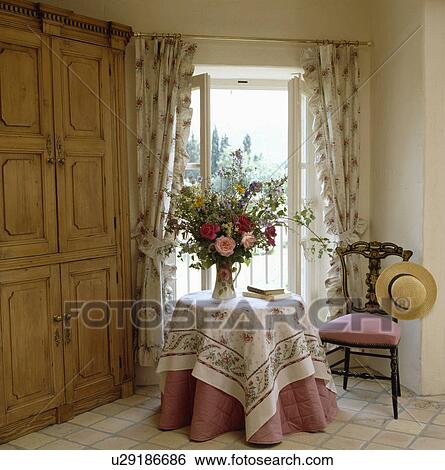 Large pine cupboard beside circular table with floral and pink cloths in front of French windows with floral curtains View Large Photo Image Stock Photograph - Large pine cupboard beside circular table with floral and pink cloths in front of French windows with floral curtains. Fotosearch
