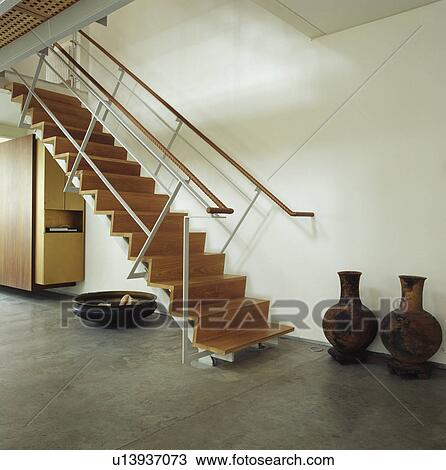 Stock Image - Large pots beside wood and metal staircase in modern white hall with stone floor. Fotosearch