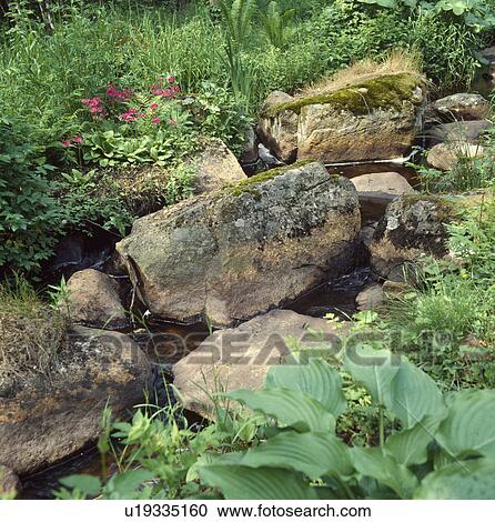 Stock Image - Large rocks beside stream in country garden. Fotosearch