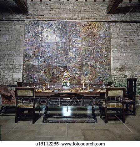 Stock Photography - Large tapestry shutters on stone wall above chairs and tables in country dining room. Fotosearch