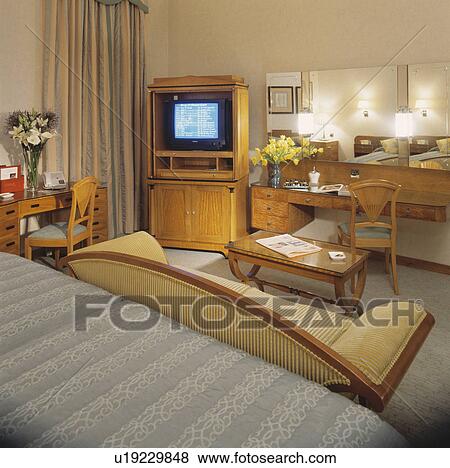 Stock Photo - Large television in cabinet in hotel bedroom with cream sofa. Fotosearch
