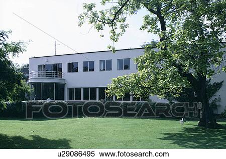 Stock Photography - Large tree on lawn in front of modern white thirties house in the country. Fotosearch