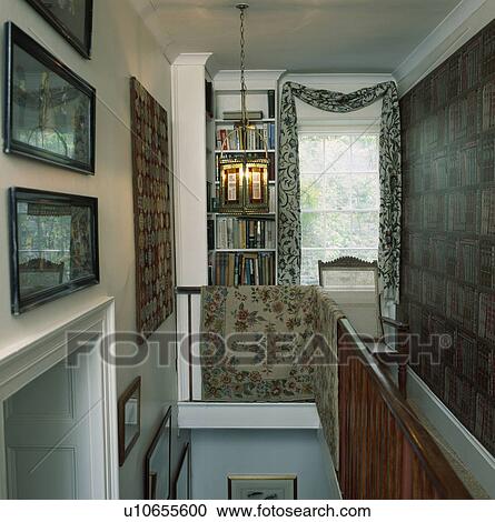 Stock Image - Lighted glass lantern above stairs in narrow landing with rug on bannisters and black+white drape above window. Fotosearch
