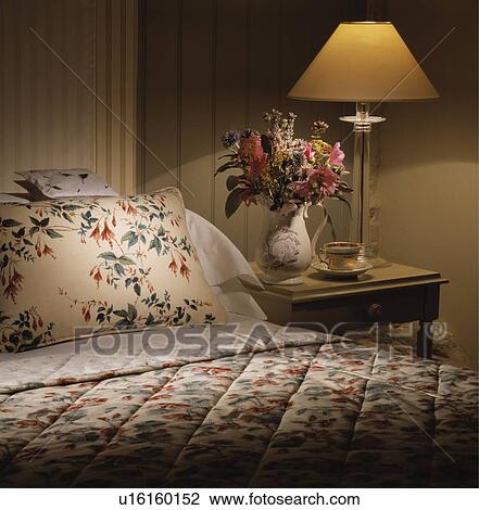 Lighted lamp beside bed with floral pillow and quilt in hotel bedroom View Large Photo Image Stock Image - Lighted lamp beside bed with floral pillow and quilt in hotel bedroom. Fotosearch