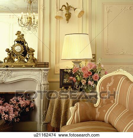 Picture - Lighted lamp on table and armchair beside fireplace in traditional living room. Fotosearch