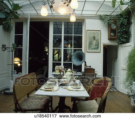Lighting tea-set on marble-topped table in dining room with cane furniture and phonograph on side-table View Large Photo Image Stock Photo - Lighting tea-set on marble-topped table in dining room with cane furniture and phonograph on side-table. Fotosearch