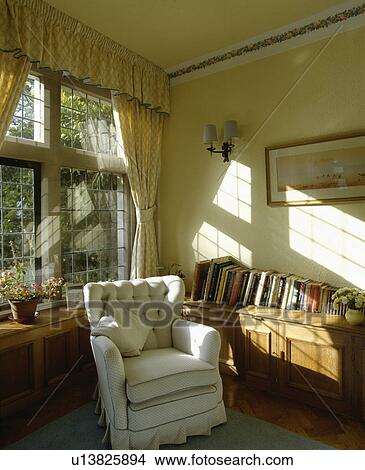 Loosecover on armchair in front of window in traditional living room View Large Photo Image Picture - Loosecover on armchair in front of window in traditional living room. Fotosearch