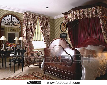 Stock Image - Mahogany half-tester bed in townhouse bedroom with large mirror above dressing table . Fotosearch