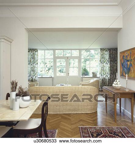 Stock Image - Marble topped table and wicker sofa in modern living and dining room with wooden parquet floor. Fotosearch