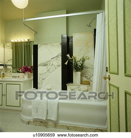 Stock Photo - Marble wall above white porcelain bath with metal shower rail and marble base in traditional pastel green bathroom . Fotosearch