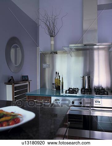 Stock Image - Mauve contemporary wooden kitchen with stainless steel hob and blue glass counter with stainless steel splash back.. Fotosearch
