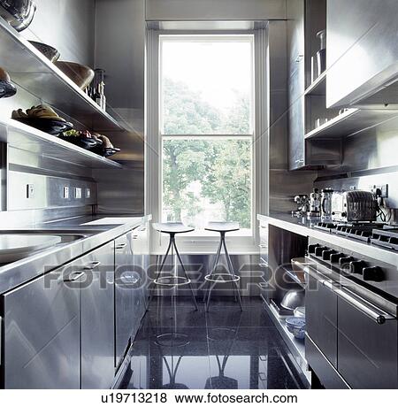Metal stools in front of tall window in modern kitchen with stainless steel fitted cupboards and polished slate floor View Large Photo Image Stock Photo - Metal stools in front of tall window in modern kitchen with stainless steel fitted cupboards and polished slate floor. Fotosearch