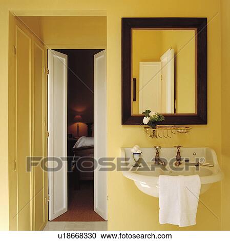 Stock Image - Mirror above wall-mounted basin beside doorway in yellow ensuite bathroom. Fotosearch