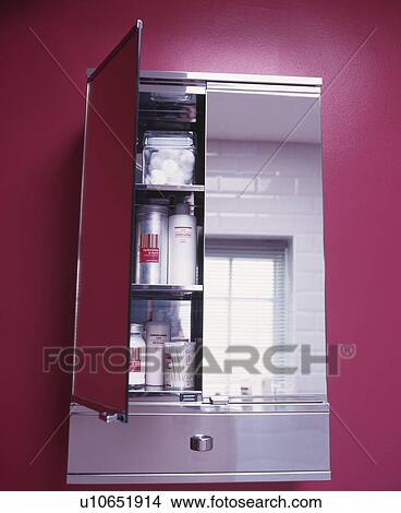 Picture - Mirrored bathroom cabinet with open door against pink wall.. Fotosearch