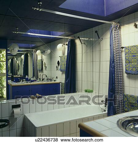 Mirrored Wall Above Bath With Shower In White Tiled Bathroom With Blue Ceiling Stock Photo