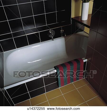 Modern black tiled bathroom with white bath and ochre floor tiles View Large Photo Image Stock Photography - Modern black tiled bathroom with white bath and ochre floor tiles. Fotosearch