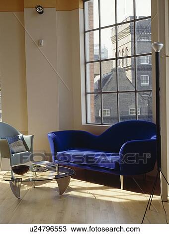 Stock Image - Modern blue sofa in front of large window in living room in converted loft with wooden flooring. Fotosearch