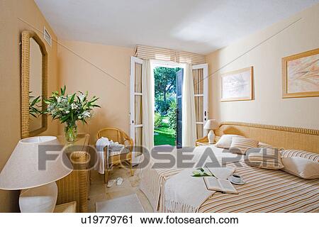 Modern neutral bedroom with wicker furniture and French windows open to garden View Large Photo Image Stock Image - Modern neutral bedroom with wicker furniture and French windows open to garden. Fotosearch