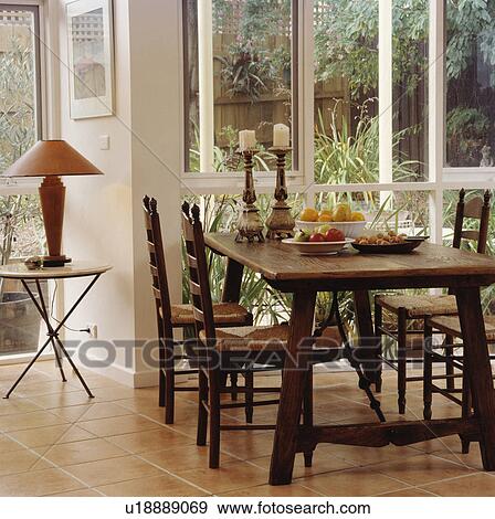 Oak dining table and rush seated chairs in diningroom with terracotta tiled floor and french windows. View Large Photo Image Stock Photo - Oak dining table and rush seated chairs in diningroom with terracotta tiled floor and french windows.. Fotosearch