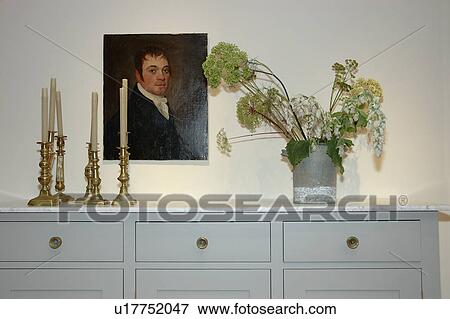 Stock Photo - Oil portrait above grey sideboard with brass candlesticks and flowers in a vase. Fotosearch