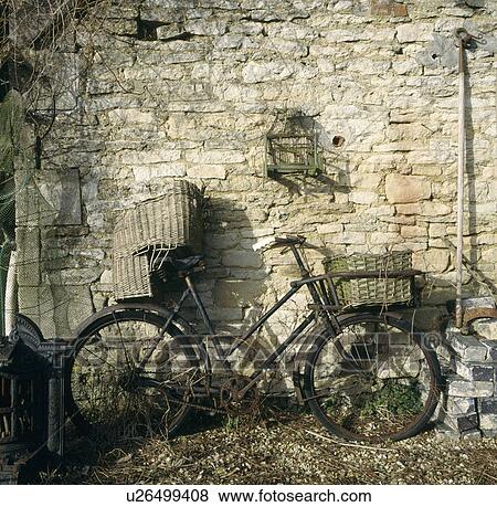 Stock Photo - Old black bicycle with basket and child's wicker seat leaning against stone wall. Fotosearch