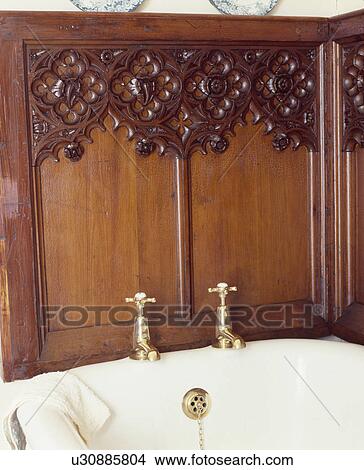 Picture - Old carved wood church panelling above white bath with brass taps. Fotosearch