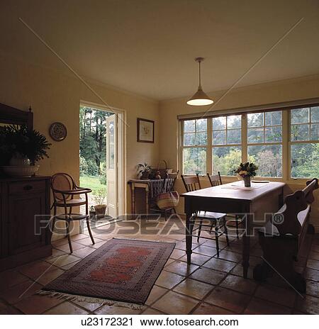 Stock Image - Old pine table and bench in cream dining room with childs highchair and terracotta tiled floor. Fotosearch