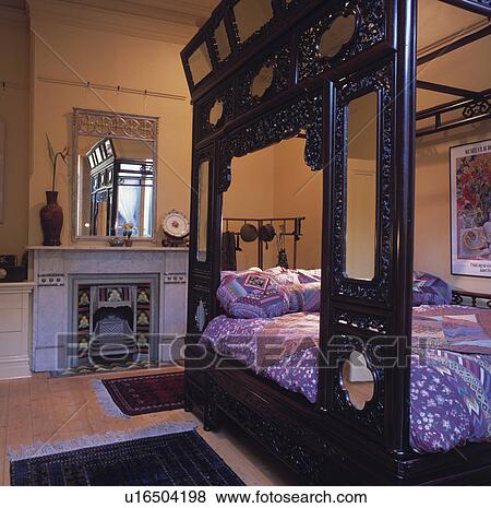 Stock Photo - Ornate carved oriental bed in bedroom with mirror above marble fireplace with tiled grate. Fotosearch