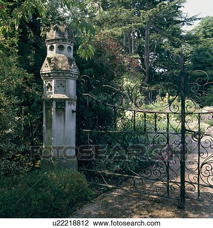 Stock Image - Ornate carved stone gatepost beside wrought iron gates in large country garden. Fotosearch