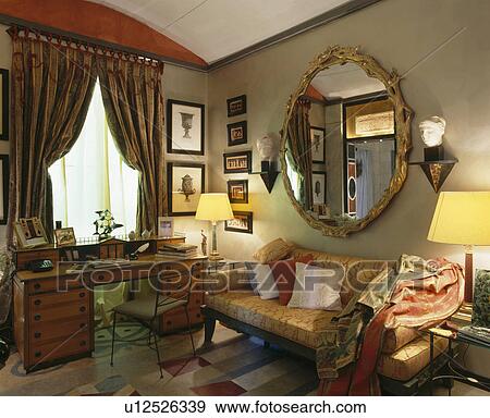 Ornate gilt circular mirror above sofa in livingroom with lighted lamps and antique desk View Large Photo Image Stock Photo - Ornate gilt circular mirror above sofa in livingroom with lighted lamps and antique desk . Fotosearch